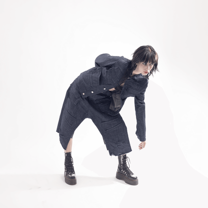 Model in dark denim outfit with deconstructed design, leaning forward dramatically against a white background.